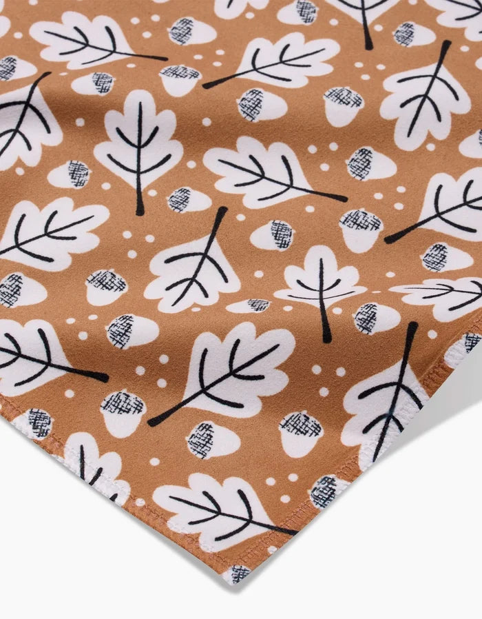 A close-up of Charlie Rowan Designs’ Falling Acorns fabric shows white oak leaves, crosshatched acorns, and small dots on brown—ideal for eco-friendly table linens or recycled napkins.