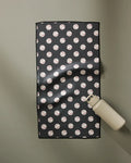 The Geometry Fastball towel, featuring a black design with a repeating baseball pattern, lies flat on a light gray surface with a beige water bottle at its lower right corner. Ultra-absorbent and fast drying, it's ideal for workouts or daily use.