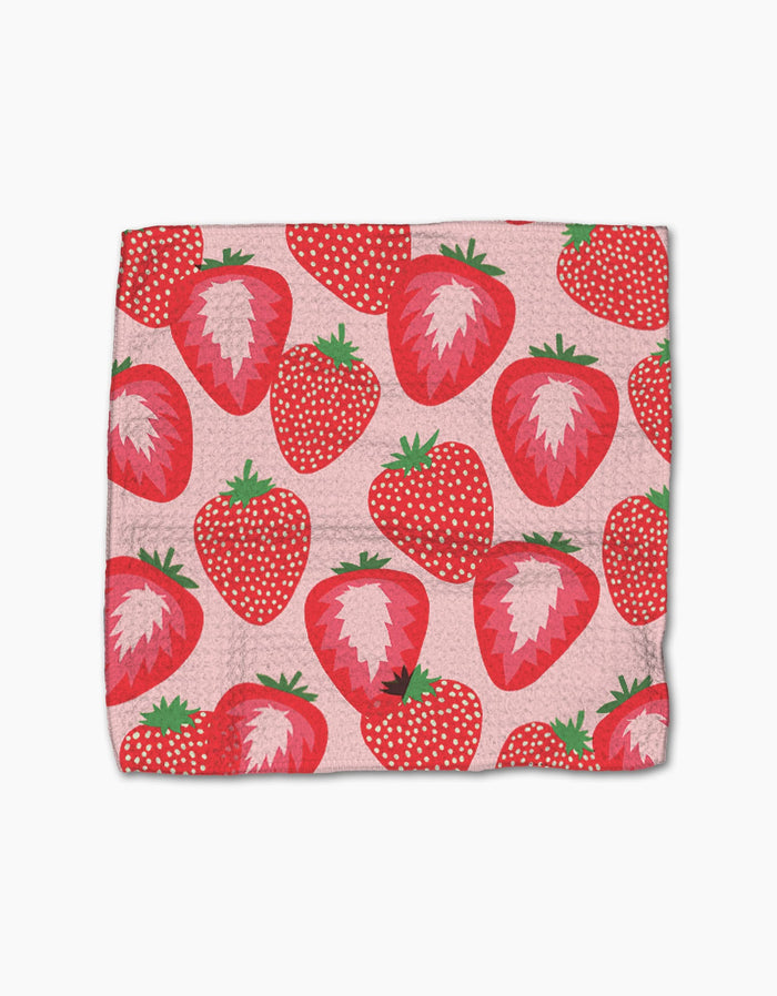 The Geometry Favorite Fruit blanket features a playful pattern of whole and sliced strawberries in red, pink, and green on a light pink background with white dots, and is crafted from recycled materials.