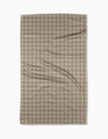 A Geometry Feelin Sandy tea towel, featuring a beige and white checkered pattern in Geoweave fabric, lies flat on a white background with gentle creases visible across its surface.