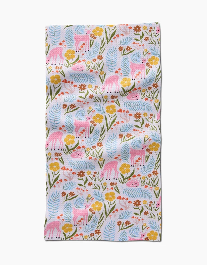 The Fern and Fawn Bar Towel by Kayla Ann features pink deer, colorful flowers, blue leaves, and green stems on white Geoweave fabric with soft folds and a playful pattern.