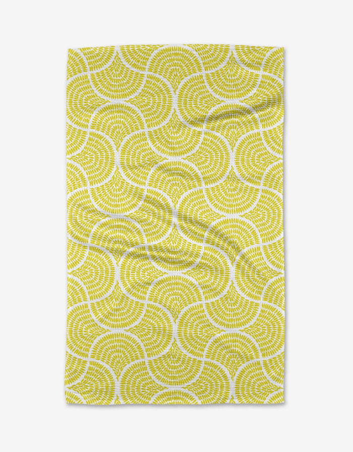 The Ferns tea towel by Dabney Lee features a repeating yellow and white wavy geometric pattern on a white background. Made from quick-drying recycled materials, the fabric has a slightly wrinkled appearance.