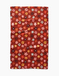 The Sara Mari Field Of Fall Daisies is a rectangular red tea towel with a pattern of small, colorful flowers in pink, yellow, blue, and orange evenly distributed across the surface.