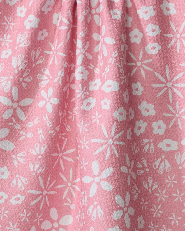 Close-up of the Hufton Studio "Fields of Flowers" tea towel, made from textured pink Geoweave fabric and adorned with a cheerful pattern of white flowers and petals in various sizes.