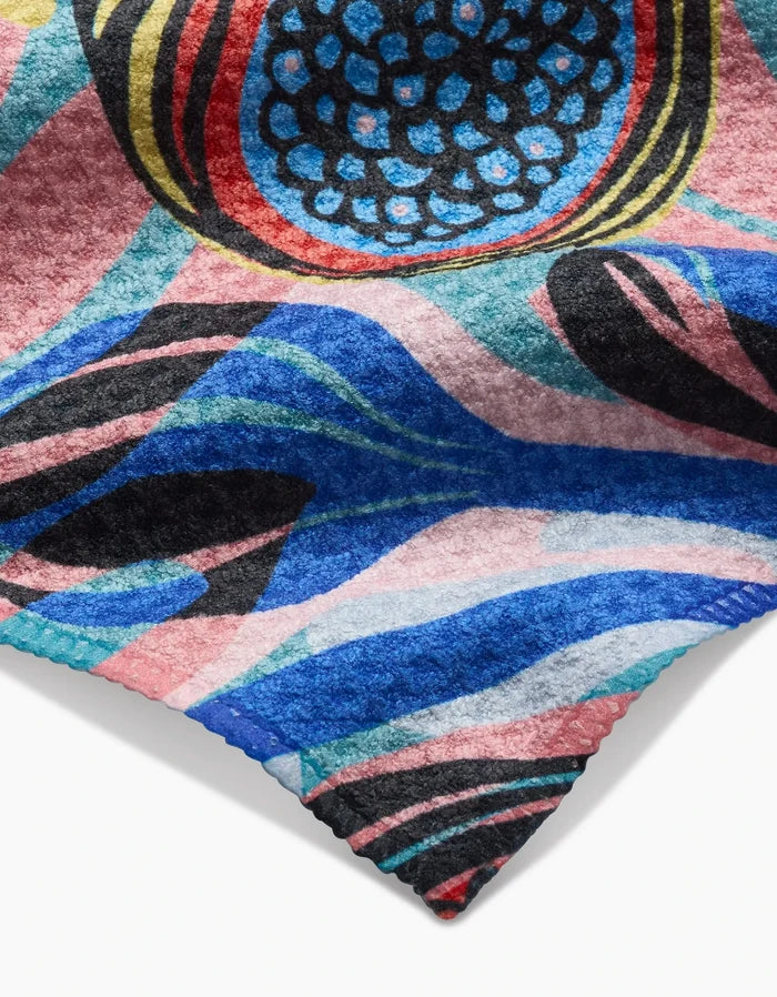 A close-up of the Fig Garden Bar Towel by Masha Volnova, made from Geoweave fabric and featuring bold abstract blue, pink, black, and red patterns with circular and wavy designs and a signature jagged edge.