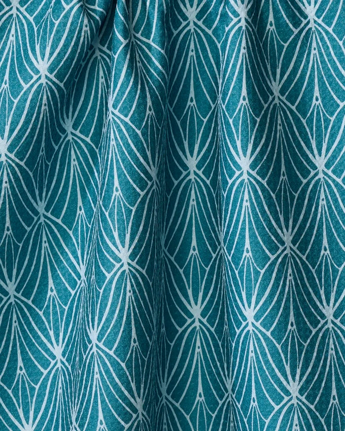 The Fish Tails tea towel by Marta Harvey features a teal fabric with a white geometric floral pattern of petal-like shapes and dots. Made from ultra-absorbent recycled materials, its gentle folds add textured shadows.