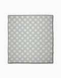 The Geometry Flora Tile Light Blue is a quick-drying beach blanket with a repeating geometric pattern of light blue hexagons and small orange circles on a white background.