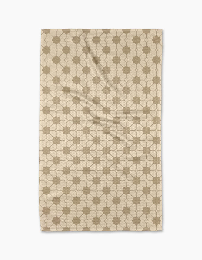 The Geometry Flora Tile Tea Towel is a beige rectangular towel with a repeating hexagon and interlocking circle pattern in light brown, displayed flat on a white background. Made from premium Geoweave fabric for superior absorbency and softness.