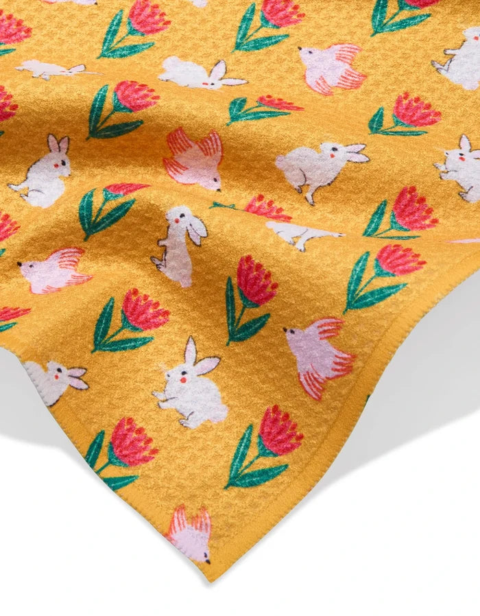 The Ceyda Alasar “Floral Bunny Parade” is a yellow ultra-absorbent towel adorned with white bunnies, pink birds, and red flowers with green leaves in a playful pattern.