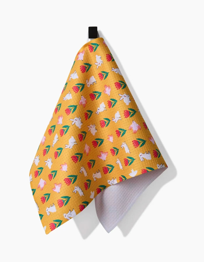 A recycled yellow kitchen towel featuring Ceyda Alasar’s Floral Bunny Parade design, with playful white bunnies and floral patterns, hanging from a black loop against a white background.