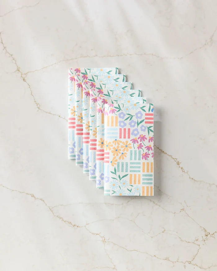 Six "Floral Garden" cloth napkins by Charlie Rowan Designs, featuring vibrant floral and geometric patterns inspired by reusable paper towels, are neatly fanned out on a white marble surface.