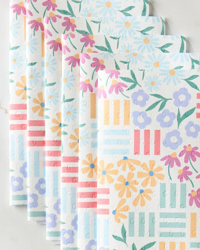 Charlie Rowan Designs’ Floral Garden eco-friendly paper towels feature vibrant flower patterns in yellow, pink, and purple with green leaves, plus red, blue, and yellow geometric stripes on a white background.