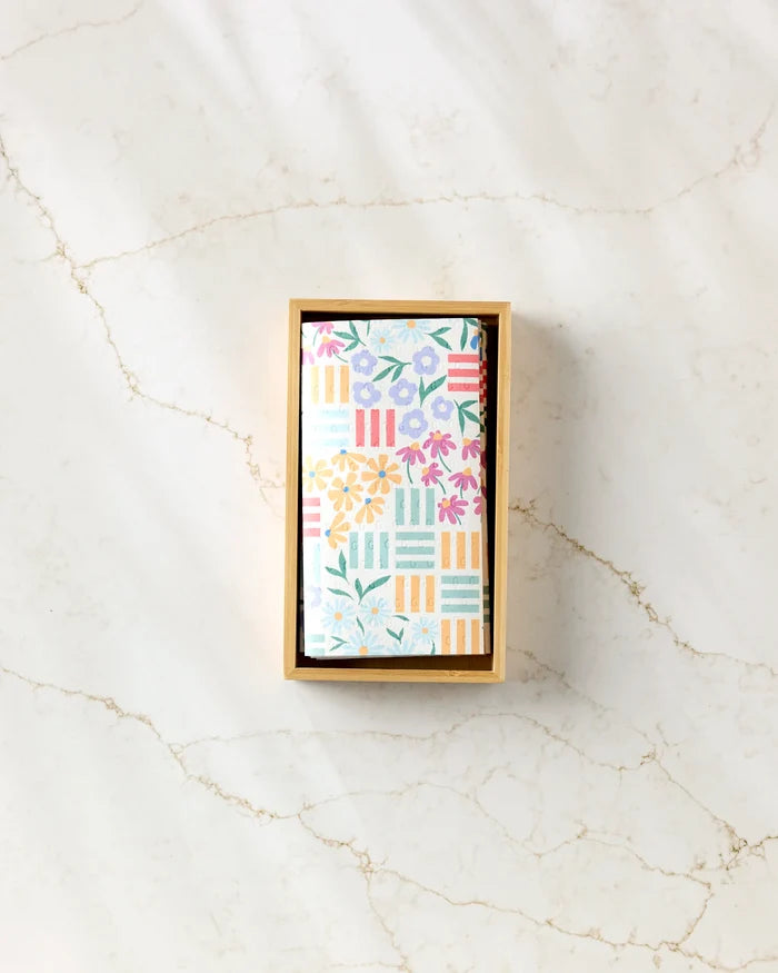 A rectangular wooden box holds Charlie Rowan Designs' Floral Garden reusable paper towels, featuring floral and striped patterns on a light, subtly veined marble surface.