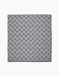 The Floral Parade Grid scarf by Geometry is a square accessory made from recycled materials, showcasing a repeating red, light blue, and dark blue geometric pattern on a light gray grid background.