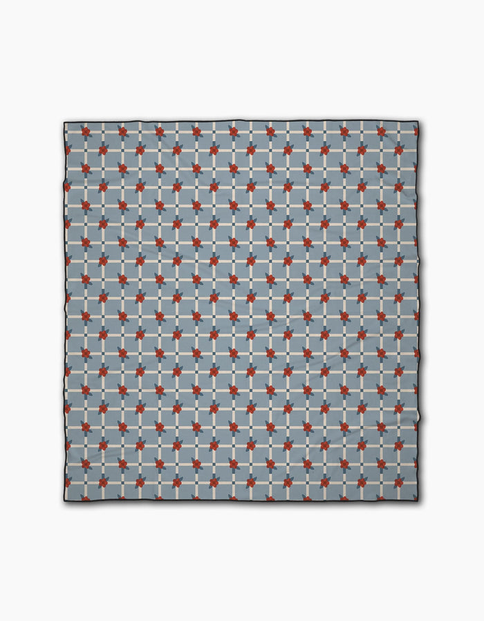 The Floral Parade Grid scarf by Geometry is a square accessory made from recycled materials, showcasing a repeating red, light blue, and dark blue geometric pattern on a light gray grid background.