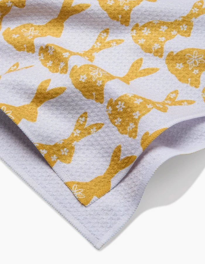 The Floral Spring Bunny tea towel by Hufton Studio features yellow bunny silhouettes with floral designs on a white textured fabric. Made from recycled materials, its ultra-absorbent with one folded corner for easy hanging.