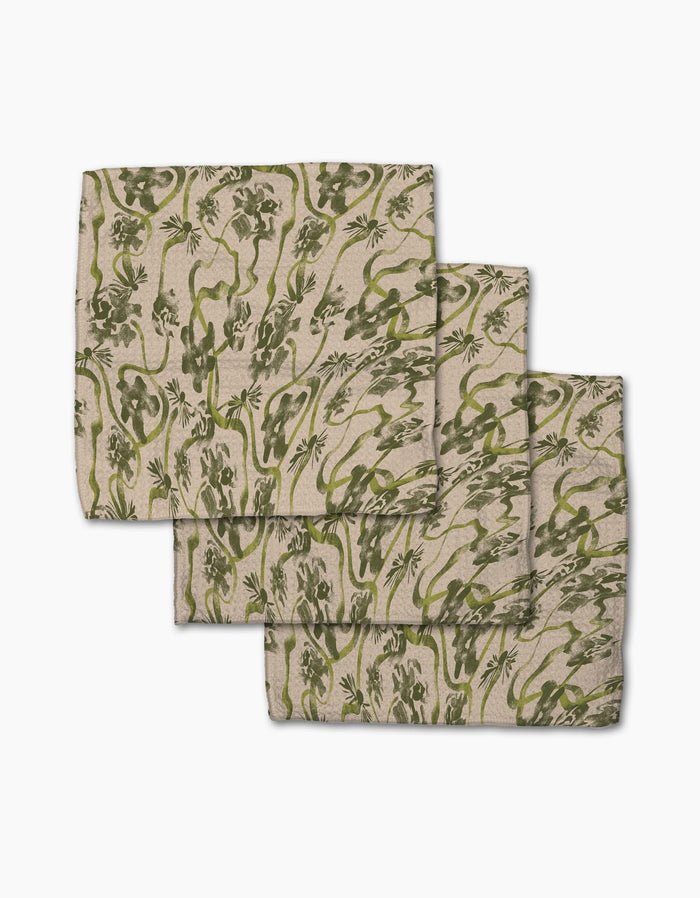 Three Floral Swirls Green cloth napkins by Geometry, made from recycled materials with a beige base and olive green floral print, are stacked in an overlapping arrangement on a white surface.