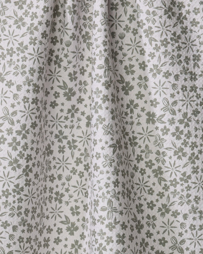 Close-up of Hufton Studio’s Flourish Gardens kitchen towel—a light, absorbent fabric with a green and white floral pattern featuring small flowers, leaves, and stems. The towel hangs softly in gentle folds.