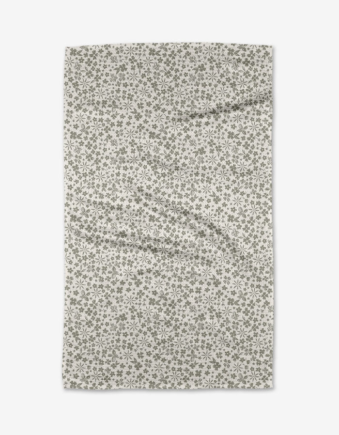 The Flourish Gardens tea towel by Hufton Studio features a rectangular beige Geoweave fabric with a small, repeating green floral pattern, displayed flat on a white background with subtle folds and wrinkles.