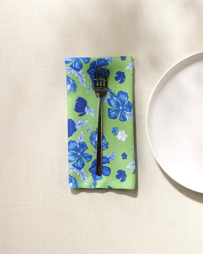 A fork sits on a GEOMETRY Flower Bomb reusable napkin with blue floral patterns, laid on a light textured surface next to a white plate—an ideal touch for any Dinner Napkin Set.