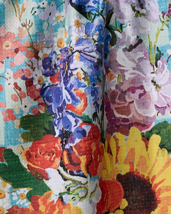 A close-up of the Flower Bouquet tea towel by Pascale Dilger, showcasing a vibrant floral pattern with sunflowers, roses, peonies, and assorted flowers in yellow, orange, pink, purple, and green.