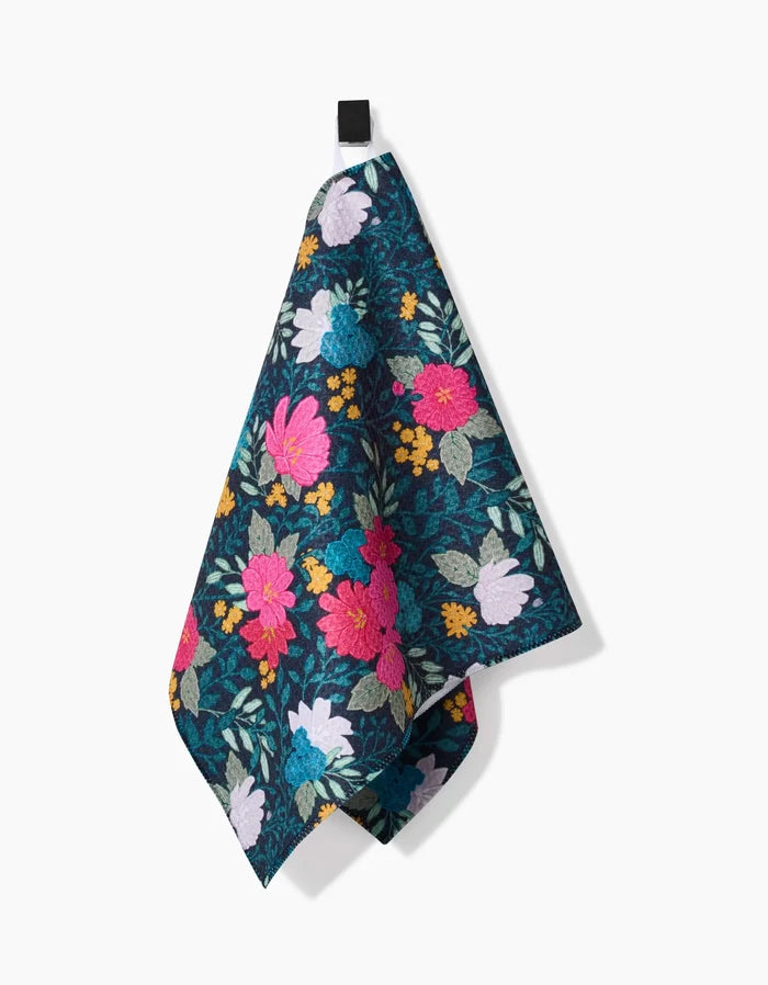 The Flower Bouquets bar towel by Katie OShea features a vibrant floral design with pink, yellow, teal, and white flowers on durable Geoweave fabric. It hangs from a black loop against a plain white background for added style and absorbency.