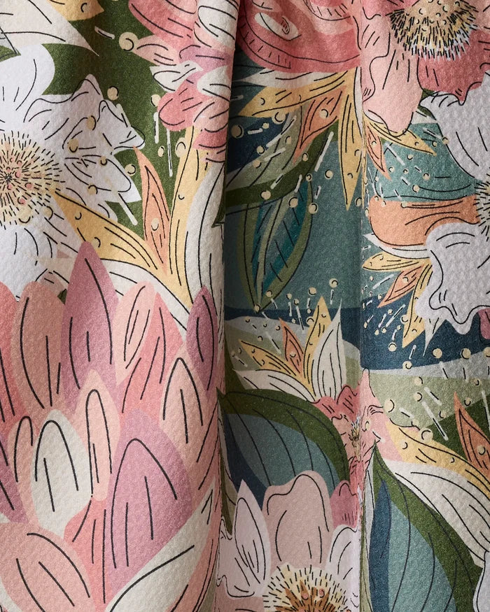 Close-up of the Flower Explosion kitchen towel by Second Nature Studio, featuring a colorful floral pattern in pink, green, white, yellow, and blue on recycled fabric with a textured surface and soft folds.