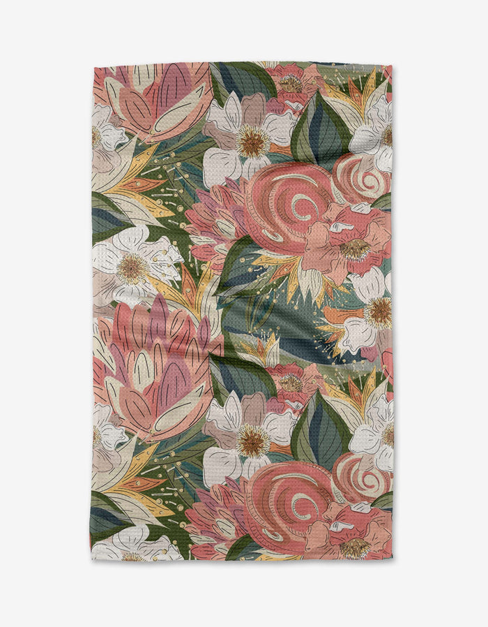 The Flower Explosion tea towel by Second Nature Studio features a vibrant floral pattern with large pink, white, and orange flowers and green leaves on textured Geoweave fabric. The rectangular cloth is shown laid flat.