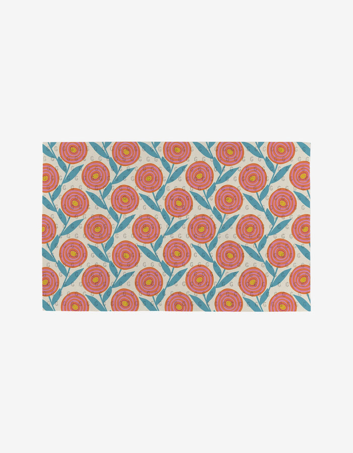 The Flower Parade rug by Lizzie Clark features a repeating pattern of stylized pink and orange flowers with green leaves on a light background. Made from post-consumer recycled materials, it’s an eco-friendly choice for your home.