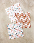 Three fast-drying Flower Patch dishtowels by Charlie Rowan Designs, made with recycled materials, are arranged on a beige surface—featuring floral, geometric grid, and leafy patterns for an eco-friendly kitchen set.