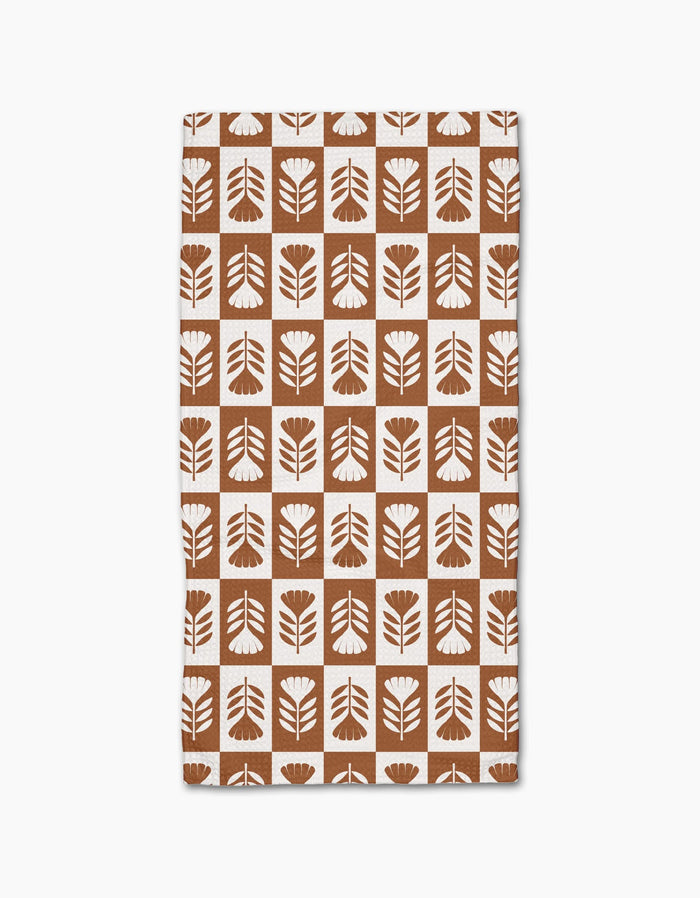 Introducing the Flower Patch bar towel by Charlie Rowan Designs—a brown and white rectangular towel made from recycled materials, featuring stylized floral shapes in a checkerboard pattern.