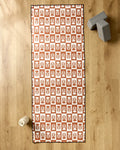 The Flower Patch yoga mat by Charlie Rowan Designs, featuring a brown and white leaf pattern, rests on a wooden floor with a white water bottle and two gray yoga blocks. A silicone grip towel boosts stability during practice.