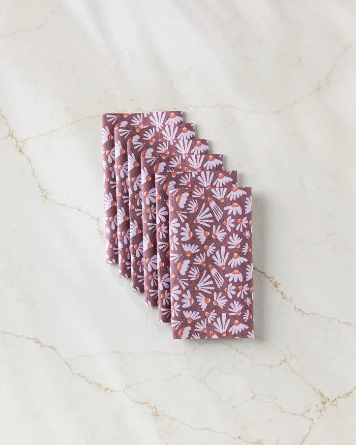 Six Flower Pop cloth napkins by Elisabeth Wing, featuring a light purple and white floral pattern on mauve, are stacked diagonally on marble—a stylish, eco-friendly alternative to kitchen and paper towels.