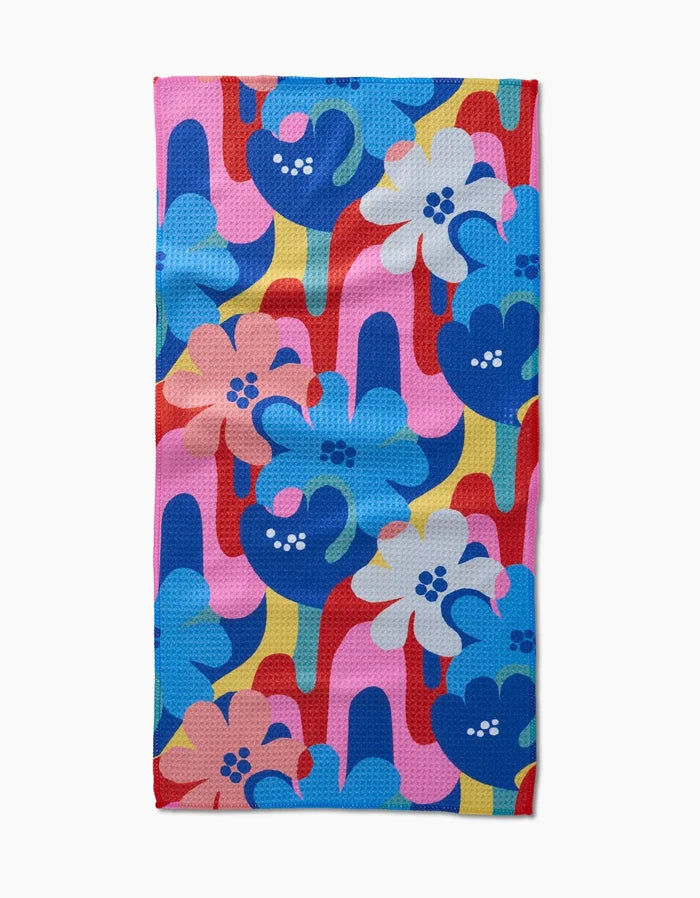 Flower Powers by Masha Volnova is a rectangular bar towel made from recycled materials, displaying bold blue, pink, white, and red flowers atop overlapping pink, yellow, red, and blue shapes.