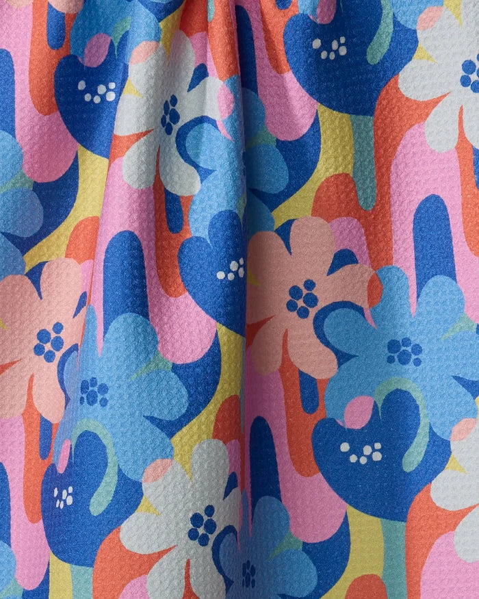 Flower Powers by Masha Volnova features a vibrant, eco-friendly tea towel with bold blue, pink, orange, and white floral patterns on textured fabric—playful shapes and wavy lines add charm using recycled materials.