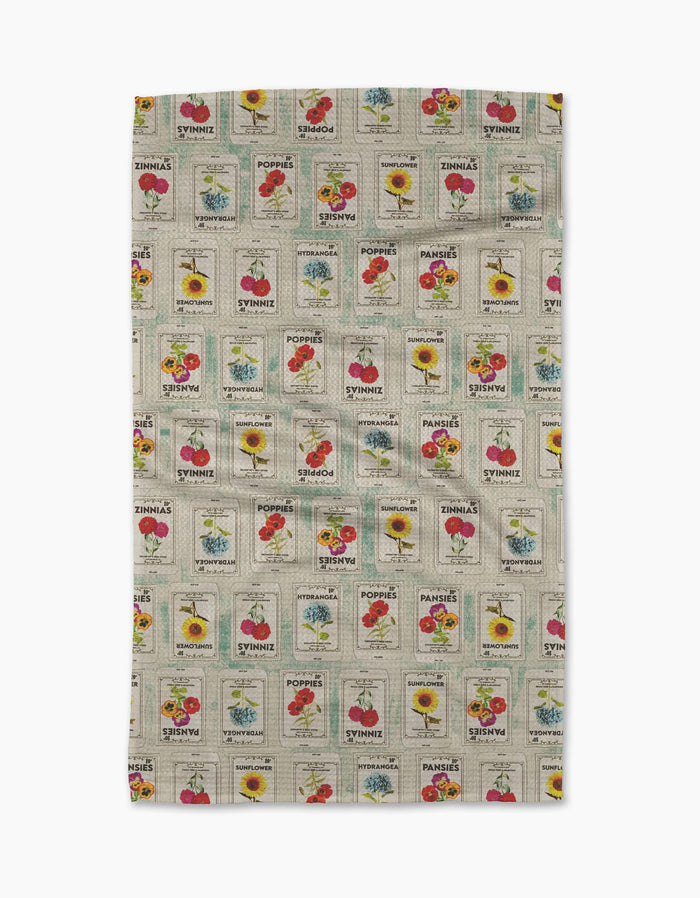 The Geometry Flower Seed Packs Tea Towel in beige features vintage-inspired tomato, poppy, sunflower, and sweet pea seed packet patterns with colorful flowers and retro text, made from ultra-absorbent recycled materials.