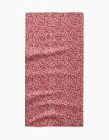 A rectangular red Flower Seeds Bar Towel by Amita Nair, featuring a repeating white leaf-like pattern, is shown laid flat with visible wrinkles and is made from ultra-absorbent Geoweave fabric.