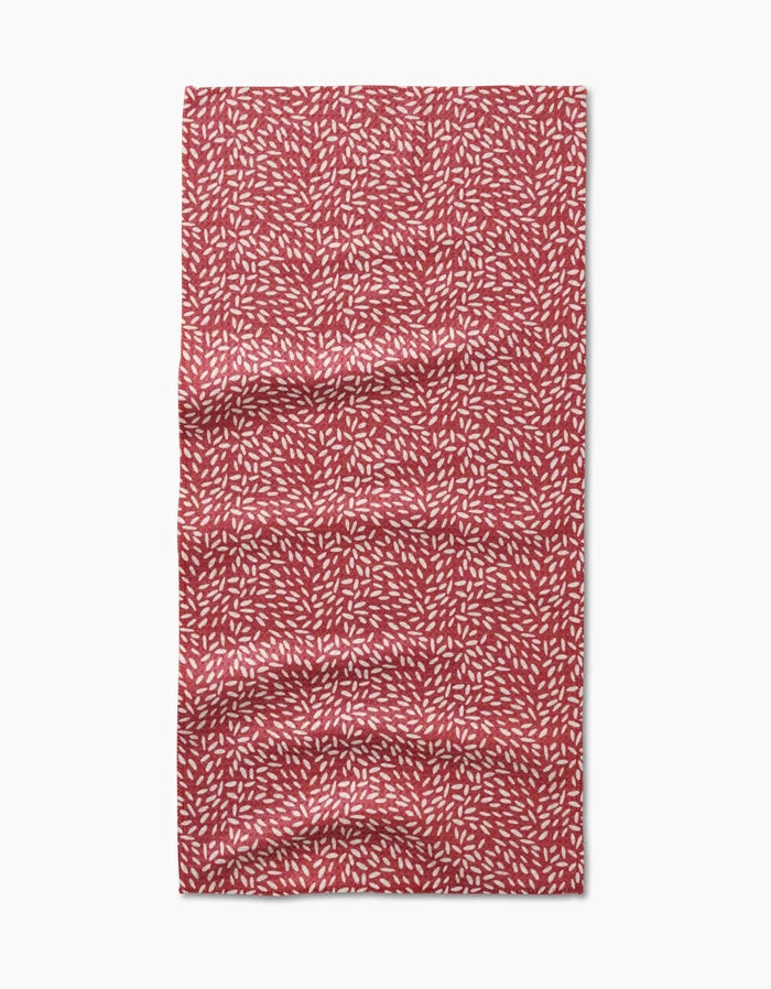 A rectangular red Flower Seeds Bar Towel by Amita Nair, featuring a repeating white leaf-like pattern, is shown laid flat with visible wrinkles and is made from ultra-absorbent Geoweave fabric.