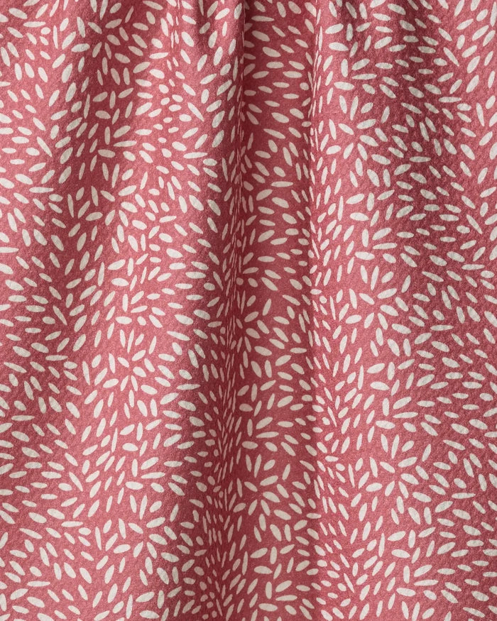 A close-up of pink packaging for Amita Nair Flower Seeds, featuring a textured surface with repeating clusters of small, white, elongated oval shapes. The soft folds and gentle shadows highlight its tactile appeal.