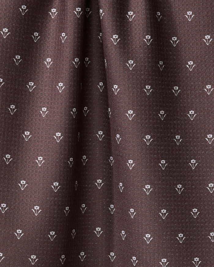 Close-up of The Buy Guide's Flowerfield Chocolate tea towel, featuring brown fabric with a repeating small white floral pattern for a subtle geometric look. This quick-drying towel appears soft and gently draped.