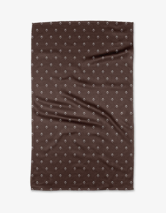 The Buy Guide’s Flowerfield Chocolate tea towel, in brown Geoweave™ fabric, displays small white diamond patterns and visible creases, shown rectangular and flat against a white background.