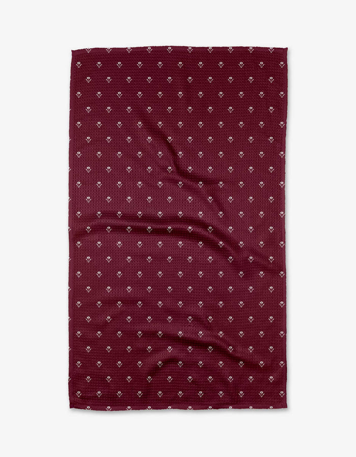 The Buy Guide’s Flowerfield Wine tea towel features a flat, rectangular maroon design with a subtle texture and repeating small white geometric pattern. Made from soft Geoweave fabric, it has slight wrinkles and is shown on a white background.