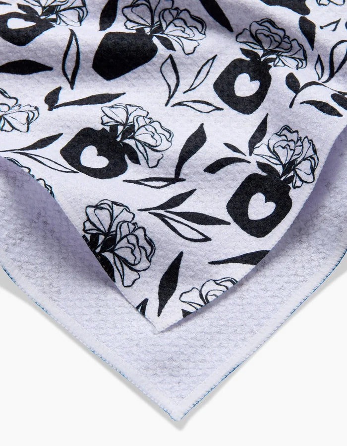 A close-up of the Flowers for Me tea towel by Charlie Rowan Designs, featuring a white background with black floral and vase patterns, including roses and hearts. The towel’s edges are neatly stitched.