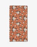 The Flowers in the Field bar towel by Charlie Rowan Designs is rectangular and rust-colored, made from Geoweave fabric, with white and light pink flowers and dark green leaves scattered across its surface.