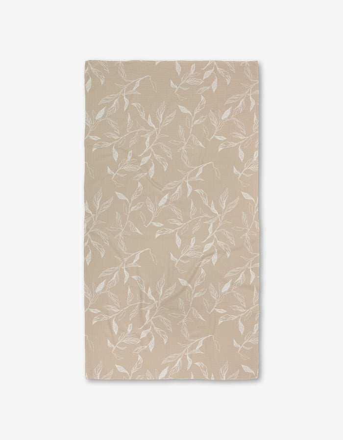 Aubrey Fairchilds Flowing Floral Luxe Bath Towel, beige and rectangular with a white leafy branch pattern and Geoweave technology, is laid flat on a white background.
