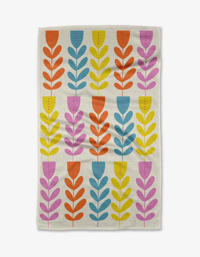 The Folk Art Tulips tea towel by Lizzie Clark is made with Geoweave fabric and features stylized tulip motifs in yellow, orange, blue, and pink arranged in vertical rows on a white background.