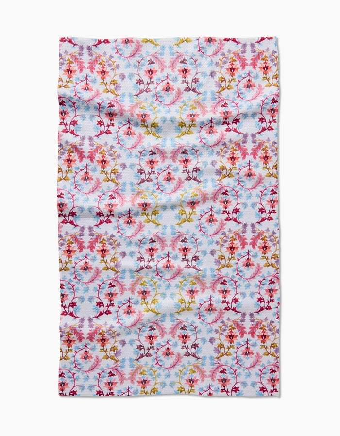 The Folk Tapestry by Maayan Alper-Swan is a rectangular cloth crafted from ultra-absorbent Geoweave fabric, featuring a symmetrical floral and branch pattern in red, pink, yellow, and purple on a blue and white background.