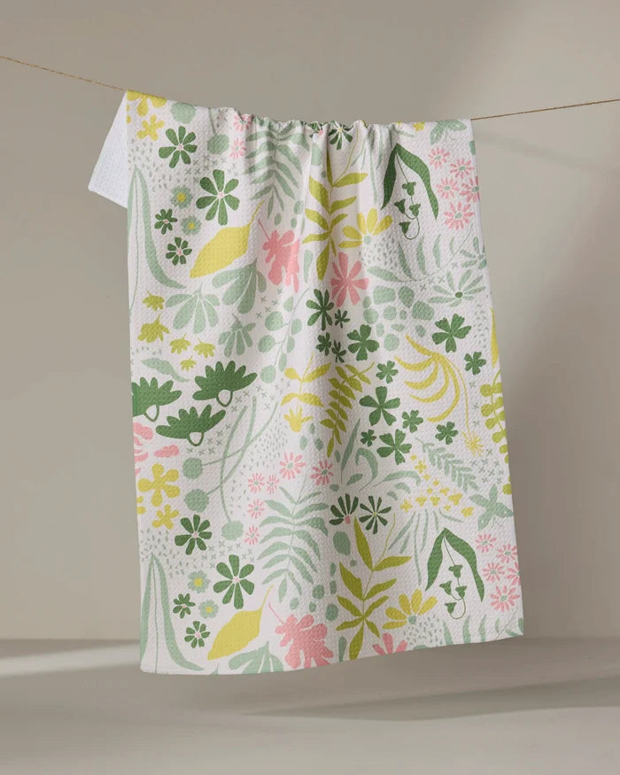 The Forager tea towel by Kayla Ann features a green, yellow, and pink floral and leaf pattern on white. Made from recycled materials, this eco-friendly kitchen accessory is shown hanging against a plain neutral background.