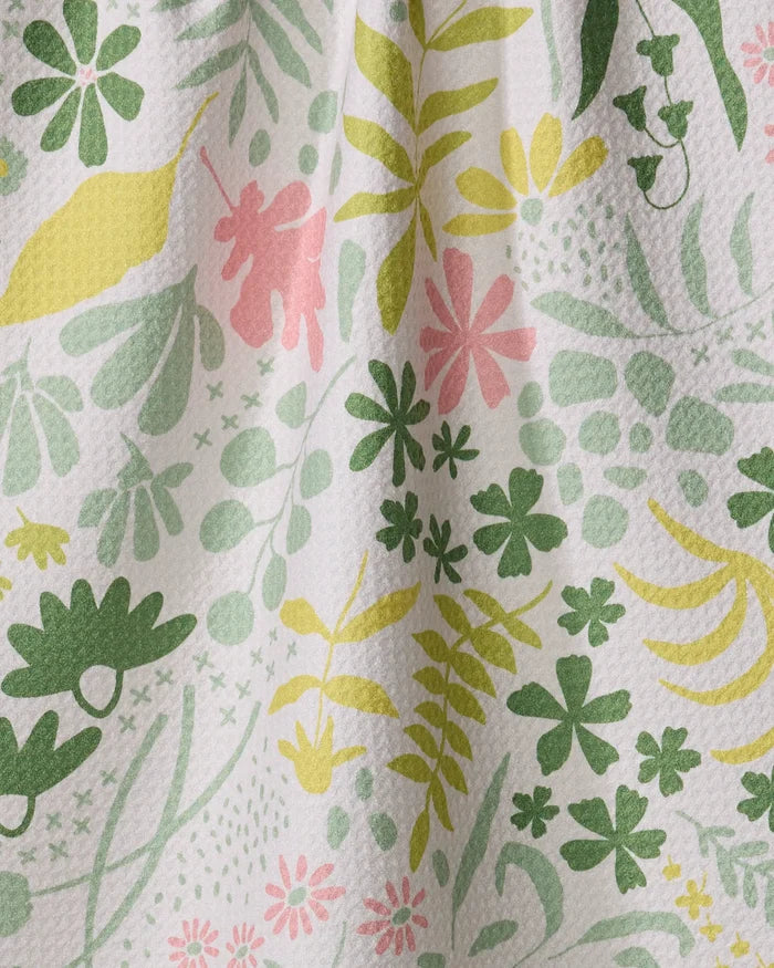 The Forager towel by Kayla Ann features textured white fabric with a vibrant floral pattern of green, yellow, and pink leaves and flowers. This ultra-absorbent towel displays visible folds and shadows for added depth.