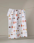 The "Foraging" recycled kitchen towel by Sara Mari, decorated with red, brown, yellow, and blue mushrooms, hangs on a clothesline against a neutral background.